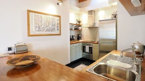 Une cuisine de taille réduite, avec une table en bois, un évier en acier inoxydable, une cuisinière et un réfrigérateur.