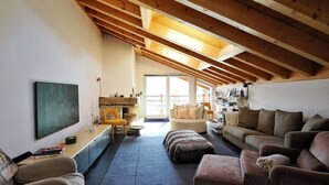Une pièce mansardée spacieuse avec un plafond haut, des poutres en bois, une cheminée en pierre, un canapé, une table basse et une bibliothèque.