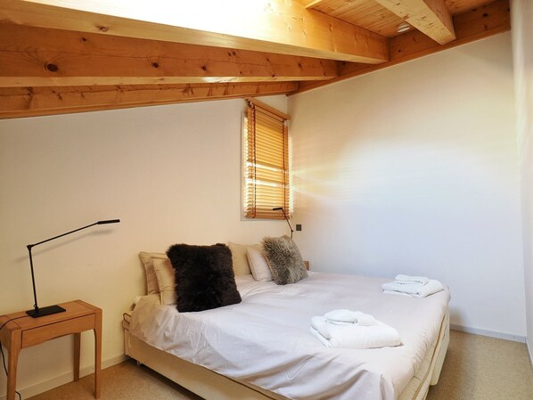 A bedroom with a bed, a bedside table, a lamp, and a window with blinds.
