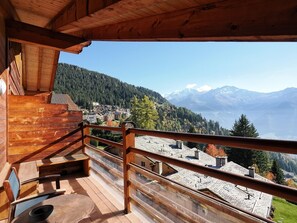 A wooden deck with a view of a mountain village and snow-capped peaks.