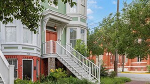 A two-story building with a red door, white railings, and a brick facade.