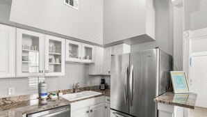 A kitchen with white cabinets, a stainless steel refrigerator, a granite countertop, and a coffee maker.