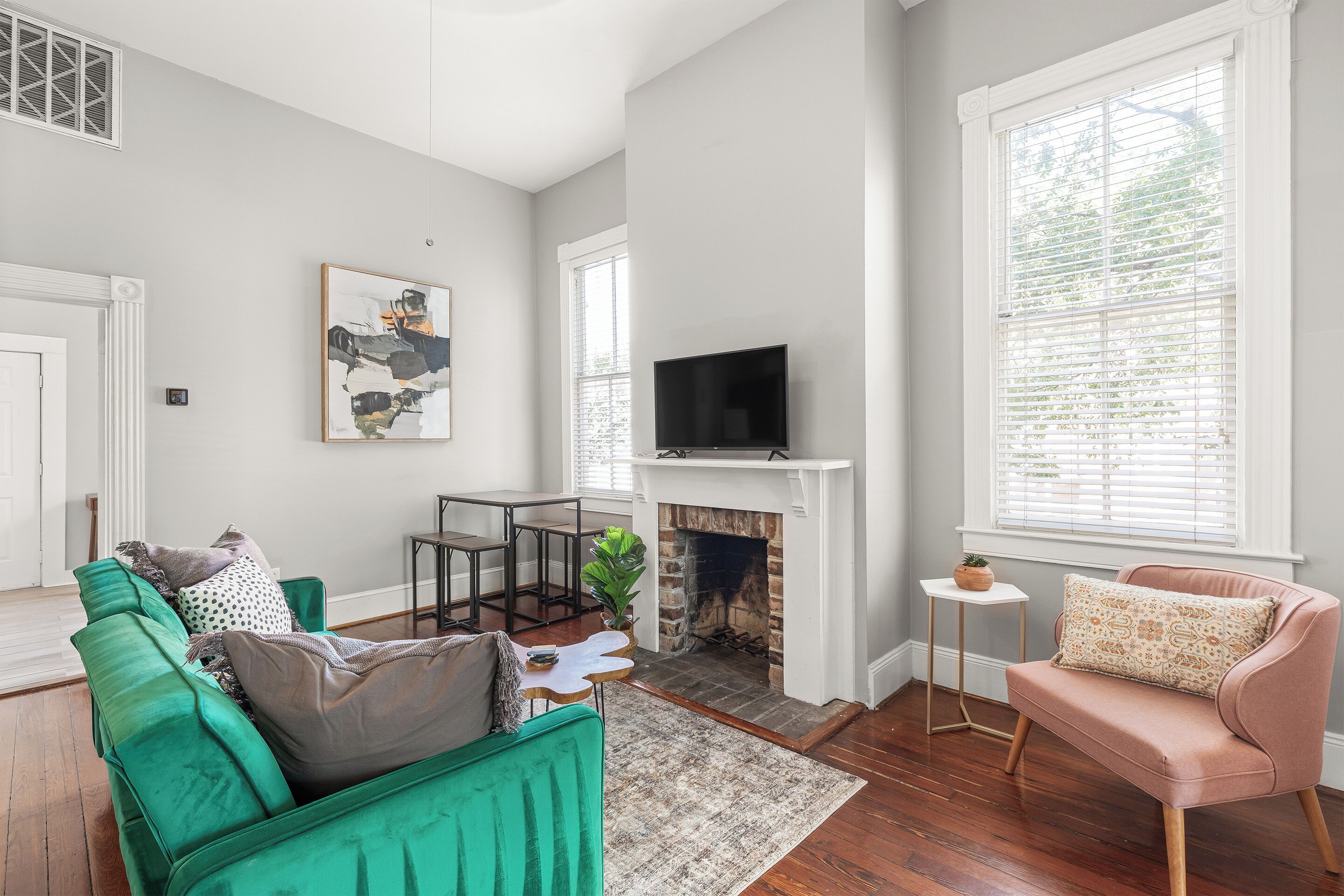A living room with a fireplace, a television, a green sofa, a pink armchair, and a dining area.