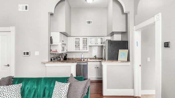 A modern kitchen with white cabinetry, a green sofa with patterned cushions, and a visible door leading to another room.