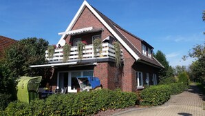 A two-story house with a sloped roof, a balcony with white railings, and a brick exterior.