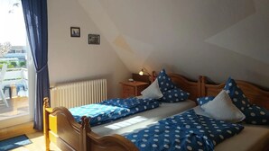 A bedroom with a sloped ceiling, a wooden bed, a bedside table with a lamp, and a view of the outside balcony.