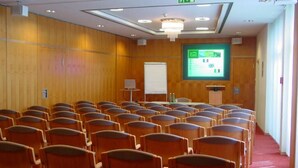 Un salón de conferencias con filas de sillas, una pizarra, una pantalla de proyector y un atril.