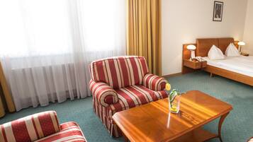 Habitación de hotel con un sofá a rayas, una mesa de centro de madera, una cama con almohadas y una mesita de noche con lámpara.