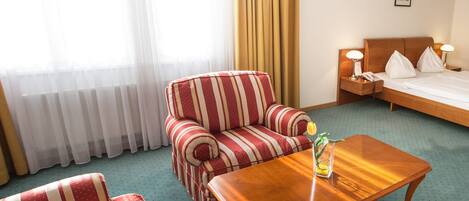 A hotel room with a striped sofa, a wooden coffee table, a bed with pillows, and a nightstand with a lamp.