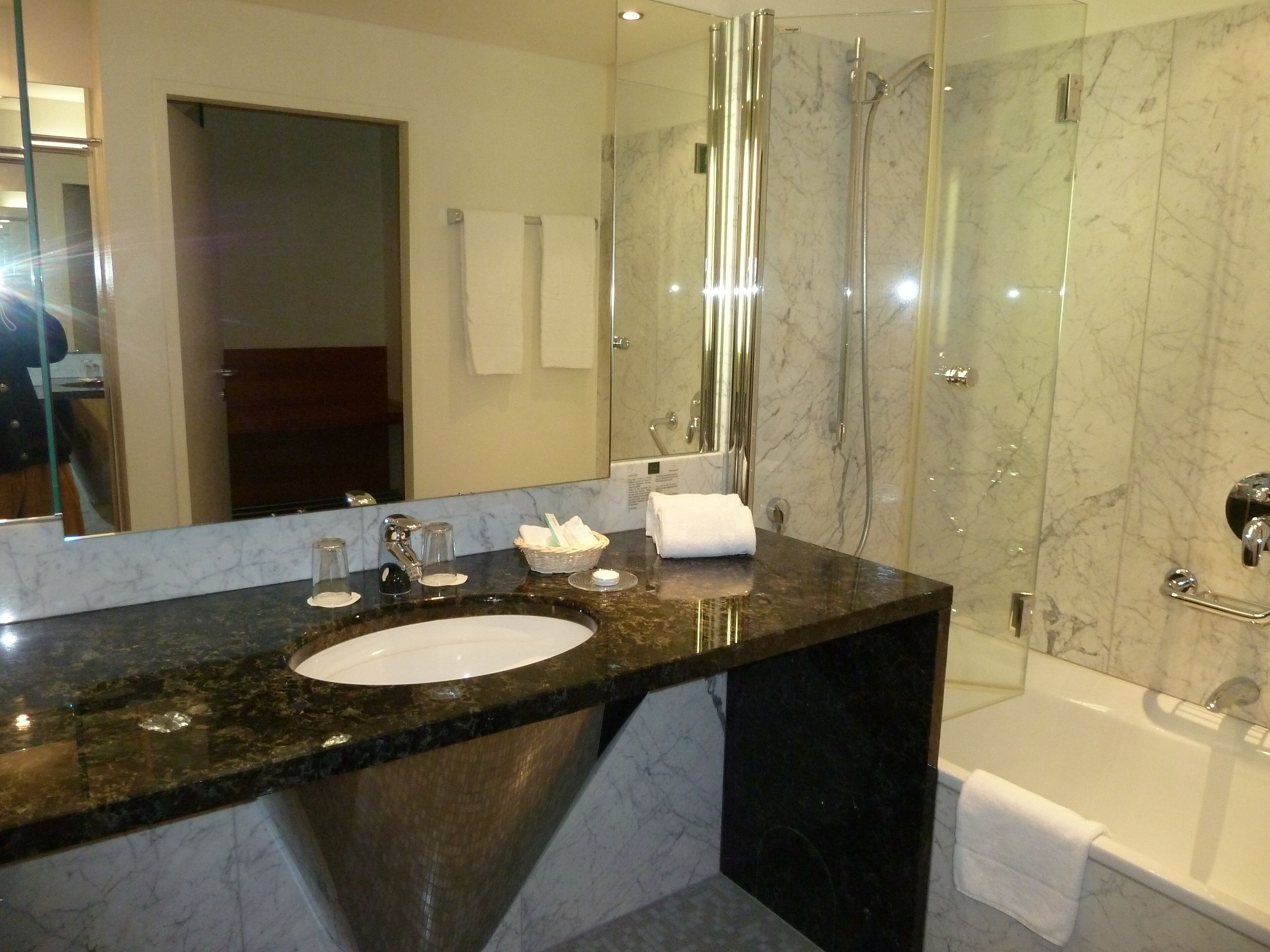 Un baño moderno con lavamanos de mármol, cabina de ducha de vidrio y bañera.