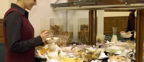 A buffet setup with various food items and a person serving themselves.