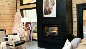 Una sala de estar acogedora con chimenea, paredes de madera, un sofá mullido y un árbol de Navidad.