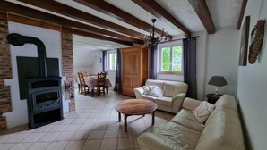 A cozy living room with a fireplace, a sofa, a dining table with chairs, and a chandelier. - Beautiful gîte in Alsace (Natzwiller)