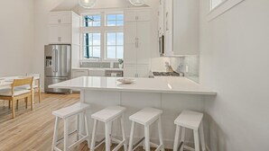 Een moderne keuken met een centraal eiland, witte kasten en barkrukken.