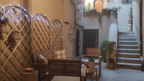 A cozy courtyard with a wooden bench and table, surrounded by potted plants and a staircase.