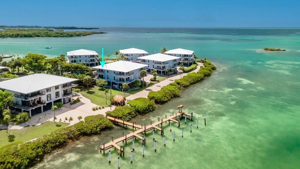 A coastal hotel with multiple white buildings, a dock, and clear turquoise waters.