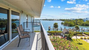 A balcony with chairs, a view of a body of water, and a dock with a thatched structure.