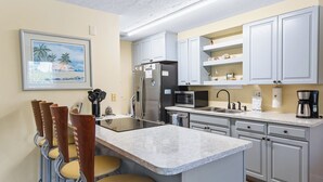 A kitchen with a central island, white cabinets, a stainless steel refrigerator, a microwave, and a coffee maker.