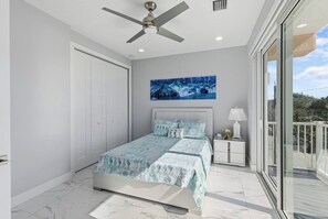 A bedroom with a bed, a ceiling fan, a nightstand, a painting, and a balcony.
