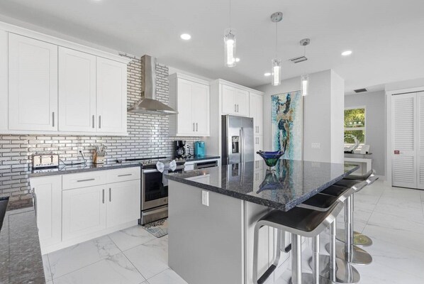A modern kitchen with white cabinets, a black countertop, stainless steel appliances, and pendant lighting.
