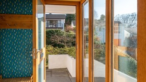 A modern interior with a wooden bench, a patterned wall, and a glass door leading to a balcony with a view of neighboring houses. - Skylark Cottage -  a single-level, two-bedroom property on the gentle slopes of Wansfell Pike, yet o (Ambleside)