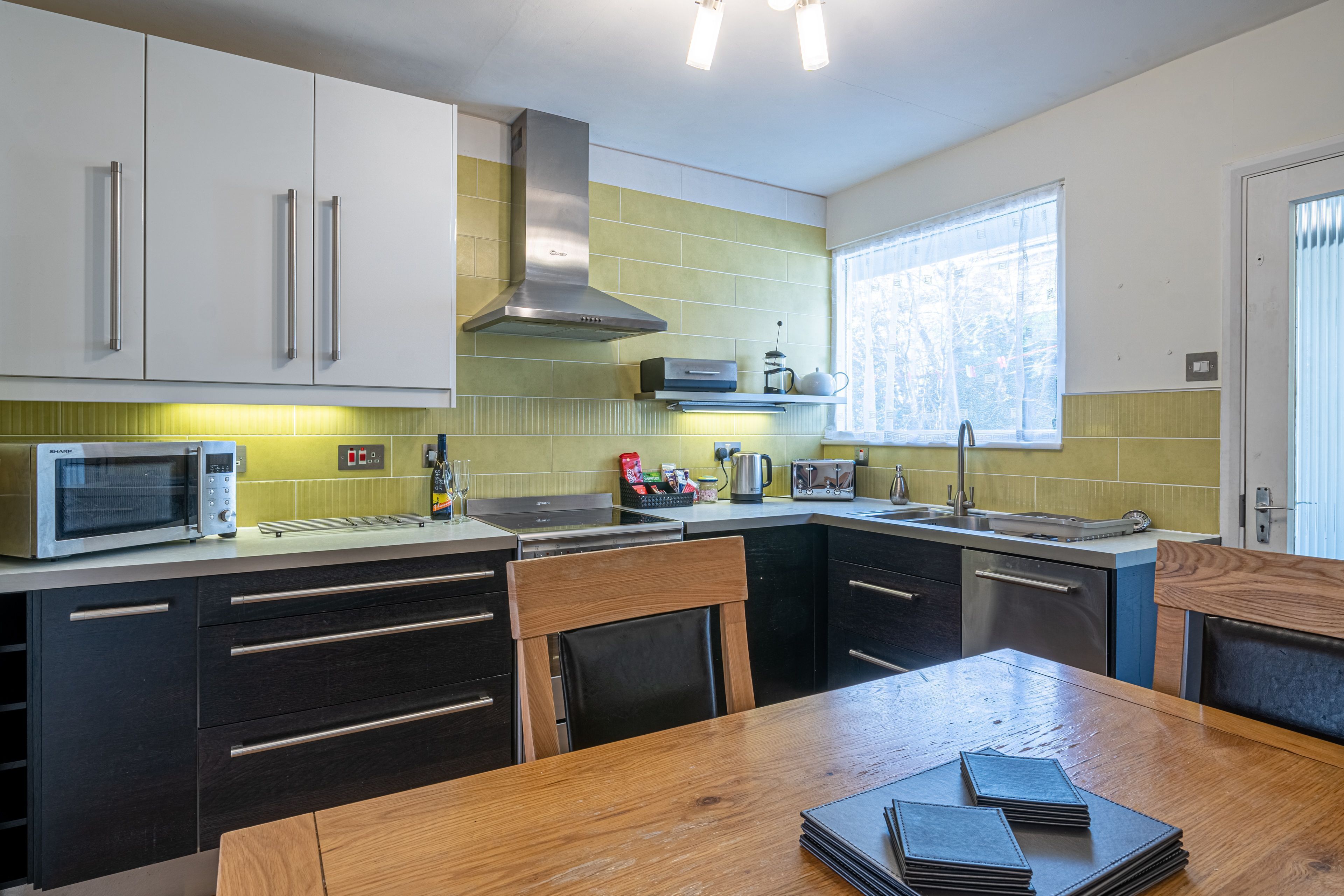 Een moderne keuken met witte kastjes, een roestvrijstalen afzuigkap, een magnetron en een spoelbak.