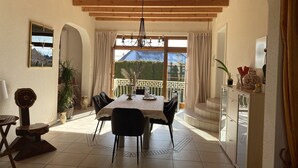 A dining area with a wooden ceiling, a table set for four, and a view of a garden through large windows.