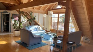 A spacious loft with wooden beams, a blue sofa, a small table, and potted plants.