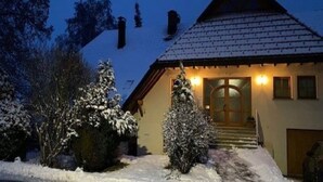 A snow-covered house with a wooden door and a small staircase leading to the entrance.