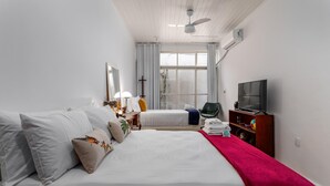 Ein Hotelzimmer mit zwei Betten, einem Fernseher, einem Schreibtisch mit Lampe und einem Fenster mit Vorhängen.