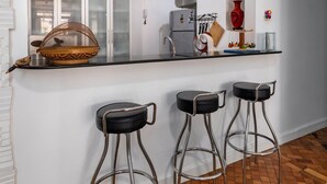 Eine moderne Küche mit schwarzem Arbeitsplatz, drei Barhocker und einem großen Spiegel darüber.