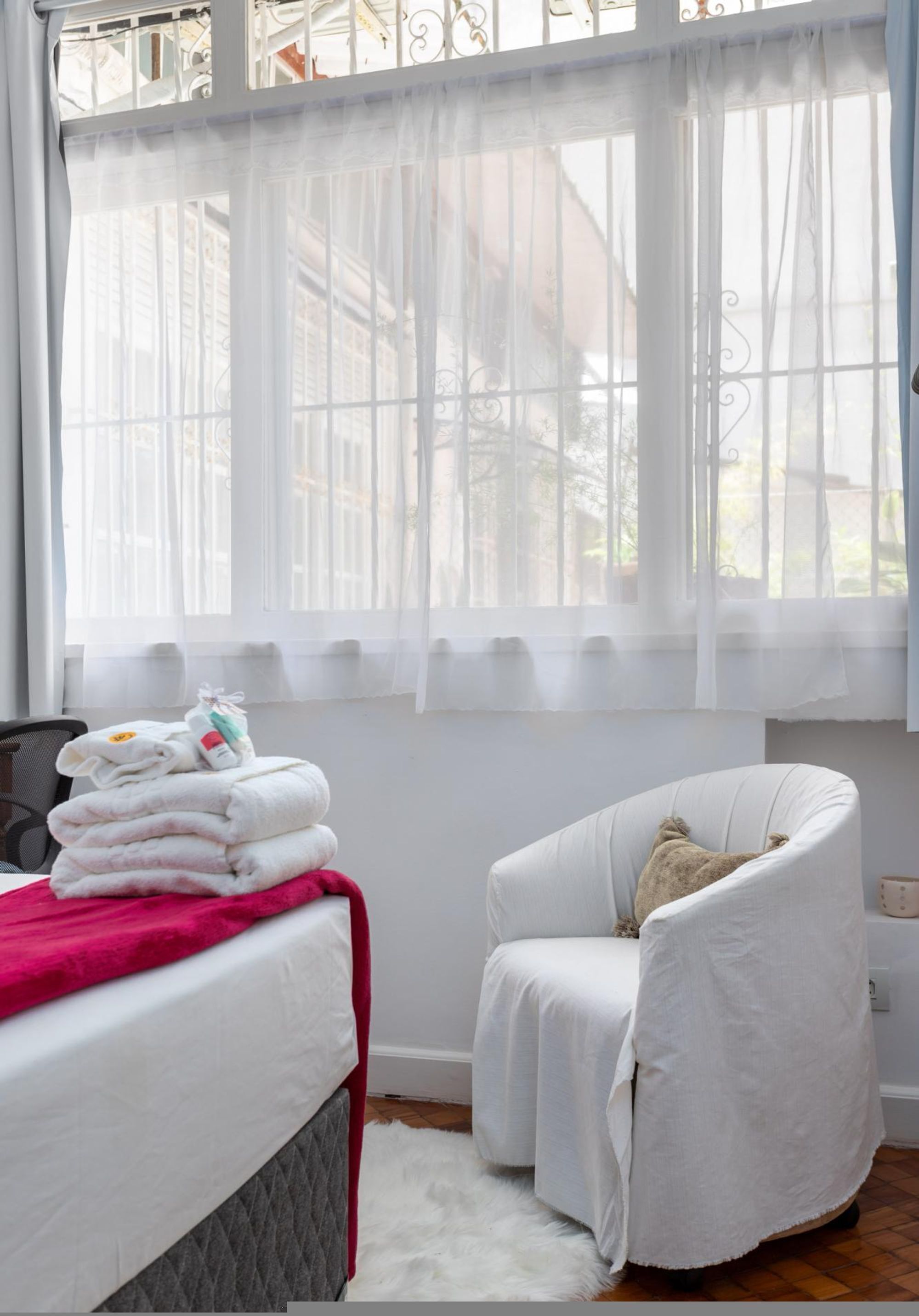 Habitación de hotel con cama, una silla, ventana con cortinas translúcidas y una pila de toallas.