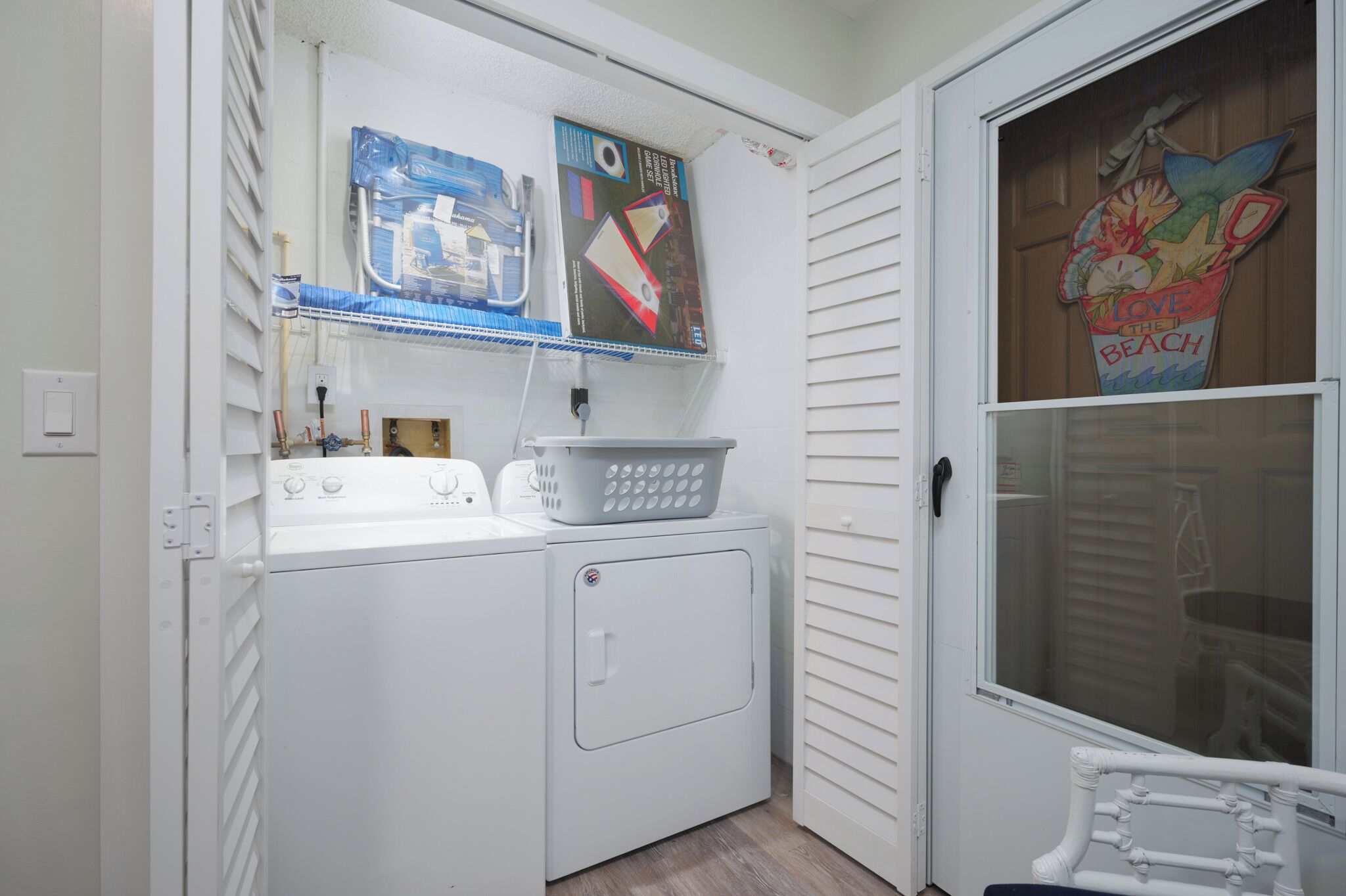 A laundry area with a washer and dryer, a basket, and a window with a beach-themed decoration.