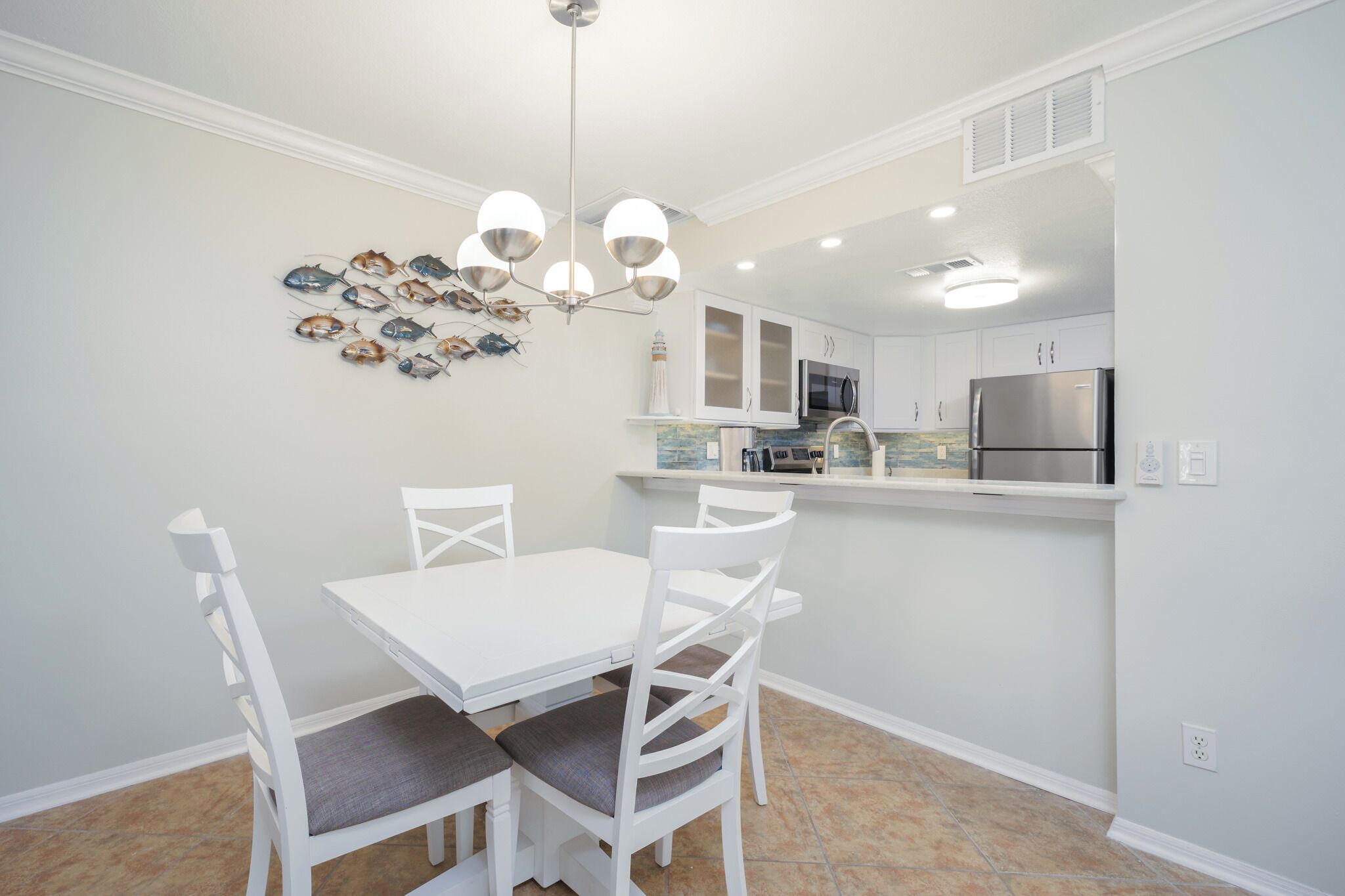 A modern kitchen with white cabinetry, a stainless steel refrigerator, and a dining area with a white table and chairs.