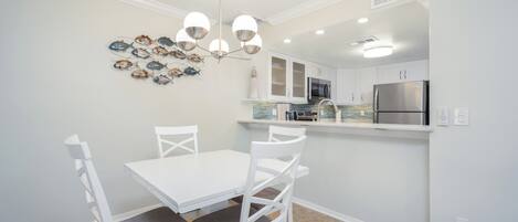 A modern kitchen with white cabinetry, a stainless steel refrigerator, and a dining area with a white table and chairs.