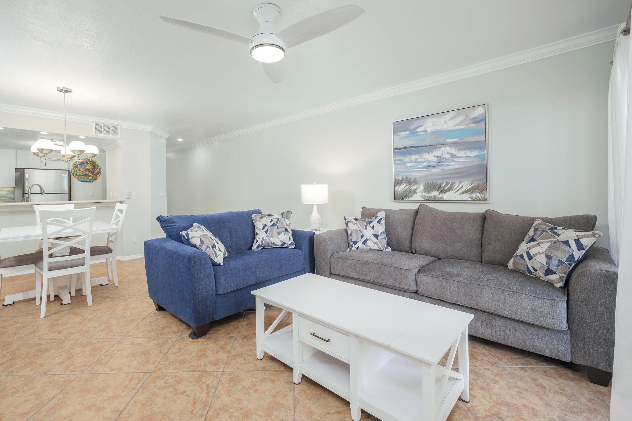 A living room with a blue sofa, a grey sofa, a white coffee table, and a dining area with a white table and chairs.