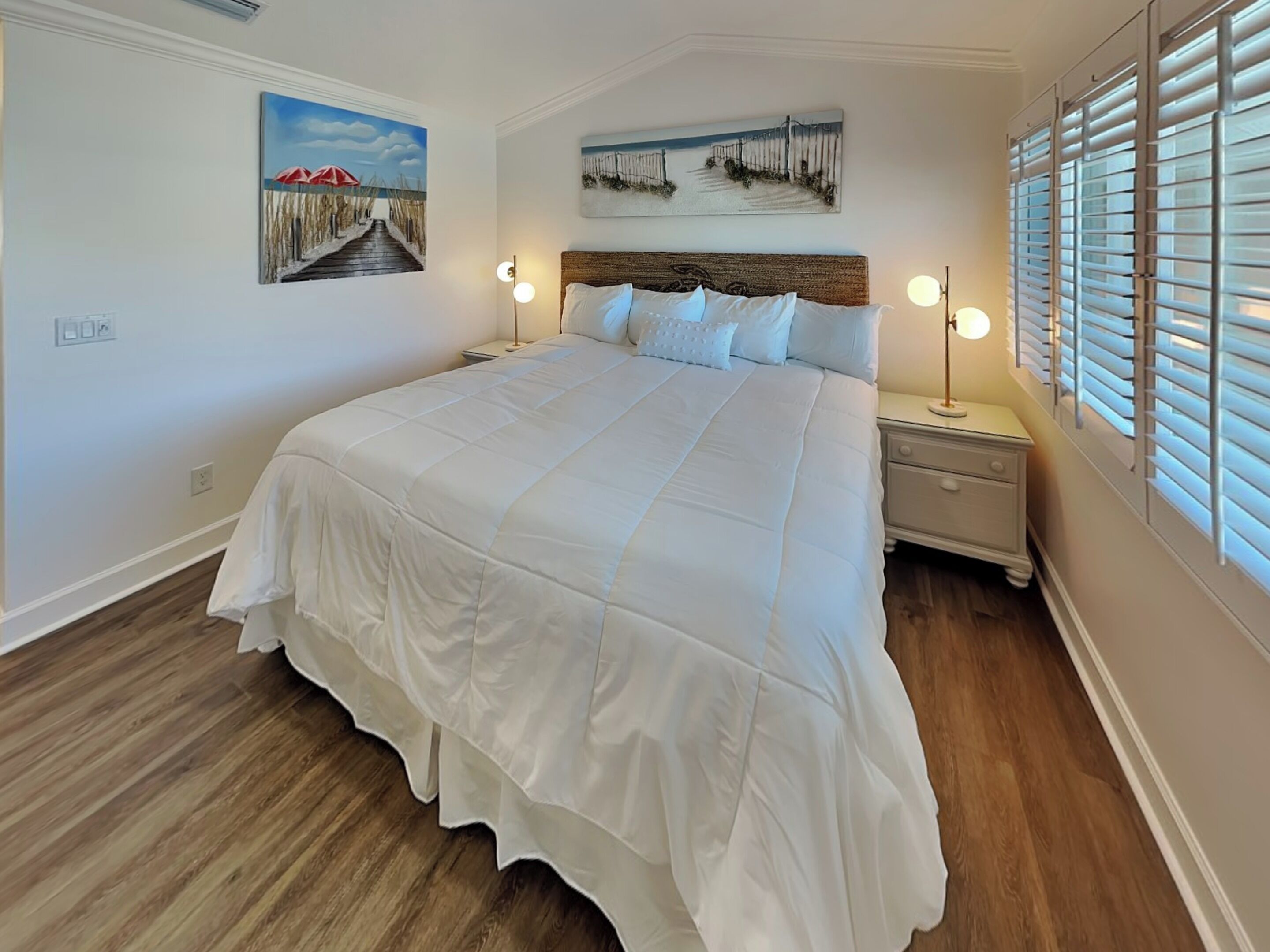 Une chambre avec un grand lit, deux tables de chevet et une fenêtre avec des stores.