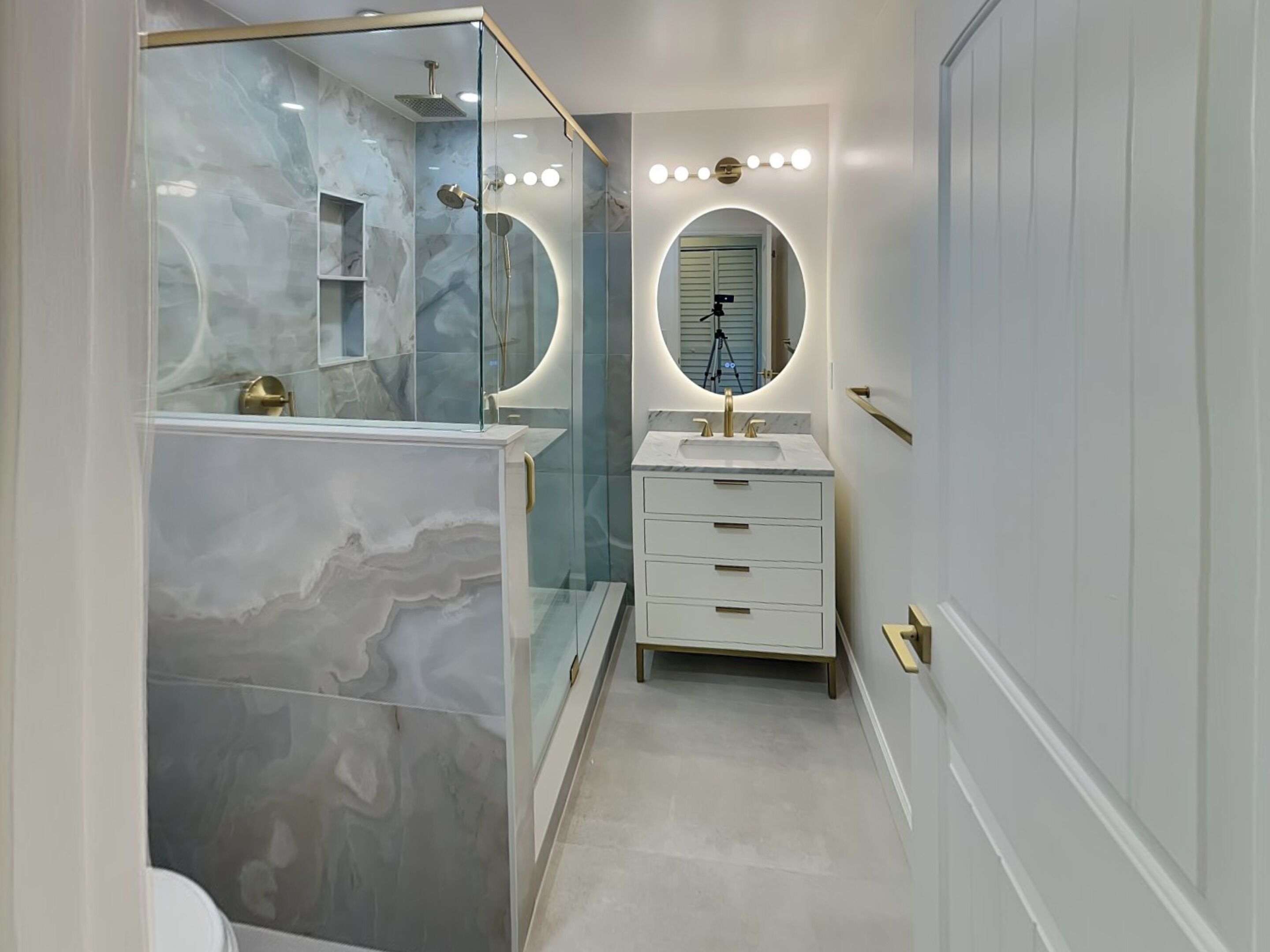 A modern bathroom with a glass-enclosed shower, a vanity with a sink, and a mirror with lights.