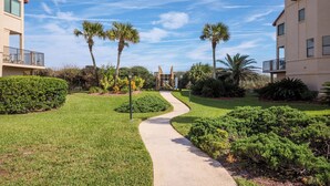 A pathway leading to a building with a clear sky and palm trees. - Spyglass 32 by Distinctive Beach Rentals (St. Augustine)