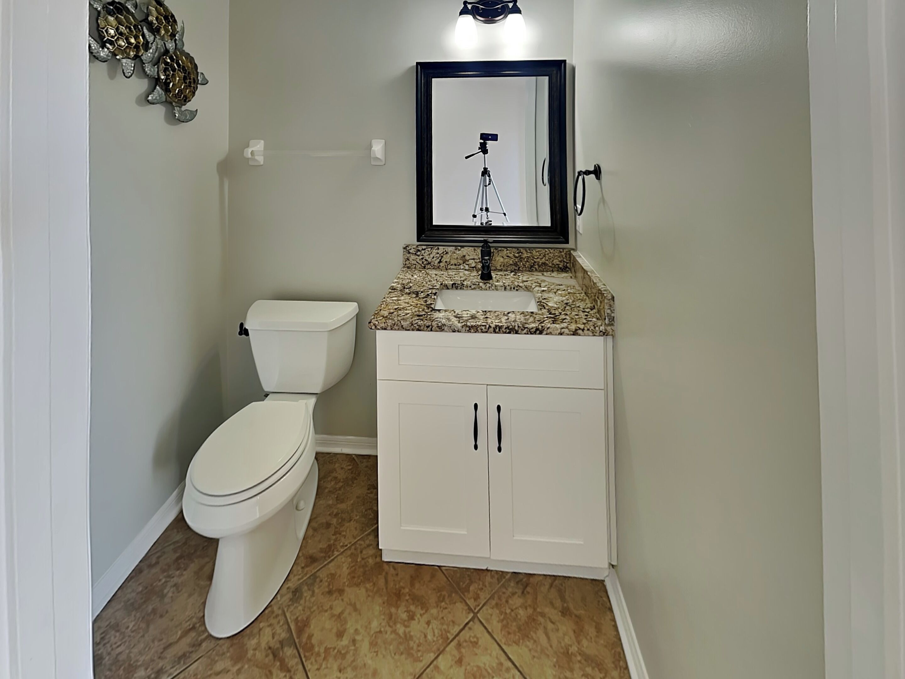 Une salle de bain avec des toilettes blanches, un lavabo sur un plan de travail en granit et un meuble blanc à deux portes.