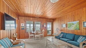 Un interior de cabaña acogedor, con paredes de madera, un sofá azul, sillas a rayas, una mesa de centro de cristal y un televisor en la pared.