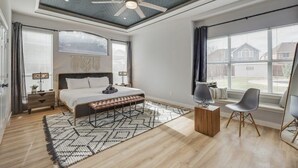 Une chambre à coucher avec un lit, un ventilateur de plafond, une grande fenêtre et une vue sur l’extérieur.