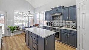 Une cuisine moderne avec des meubles de couleur sombre, un grand îlot central et une vue sur la ville grâce à de grandes fenêtres.
