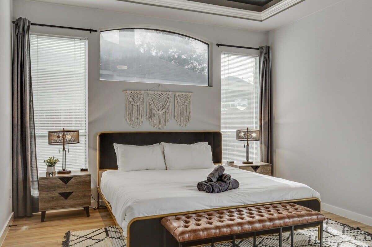 Ein Schlafzimmer mit Bett, Nachttischlampen, einer Kopfteil, einer Bank und einer Wanddekoration aus Makramee.