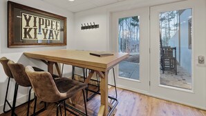 Un coin repas avec une table en bois et quatre chaises, un panneau encadré accroché au mur, et une vue sur une terrasse extérieure, visible à travers une porte vitrée.