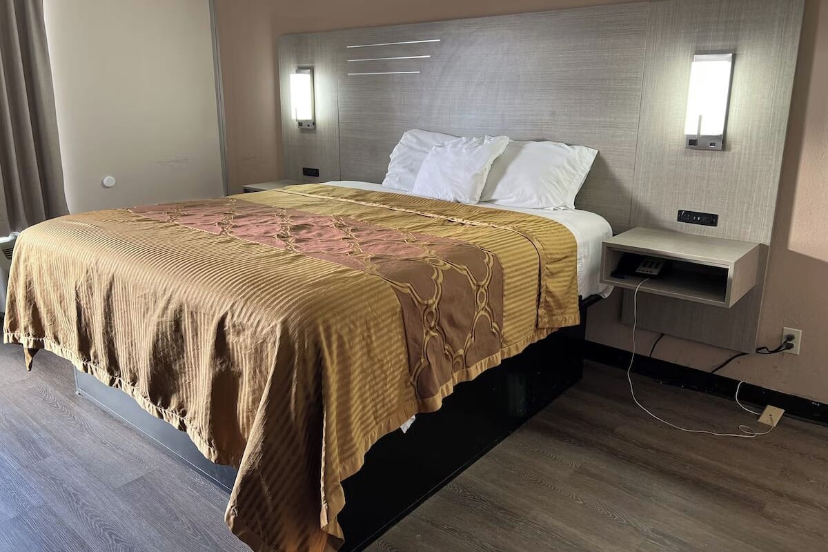 Una habitació d'hotel amb un llit gran, una taula de nit i una làmpada penjada a la paret.