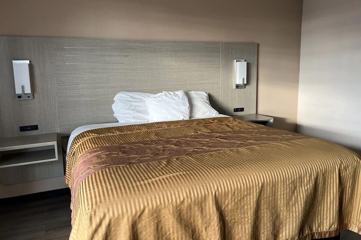 Habitació d'hotel amb un llit, una tauleta de nit i una làmpada de paret.