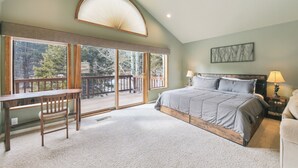 Un dormitorio con una cama grande, un escritorio y un balcón con vistas a árboles.