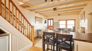 A kitchen with wooden flooring, a dining table with chairs, a staircase with wooden railings, and a window with blinds. - Host & Stay | Sea Haven (Staithes)