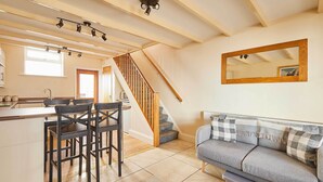 A kitchen with a central island, wooden staircase, and a grey sofa with a mirror above it. - Host & Stay | Sea Haven (Staithes)